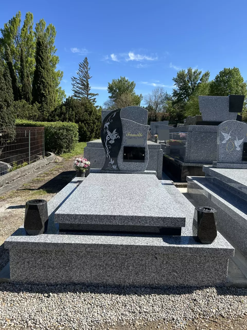 Monument funéraire en granit gris, stèle à vague en granit noir gravée d'une colombe et de rinceaux, vases assortis